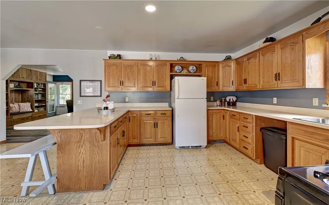 Kitchen with light floors, a peninsula, black appliances, a breakfast bar area, and light countertops