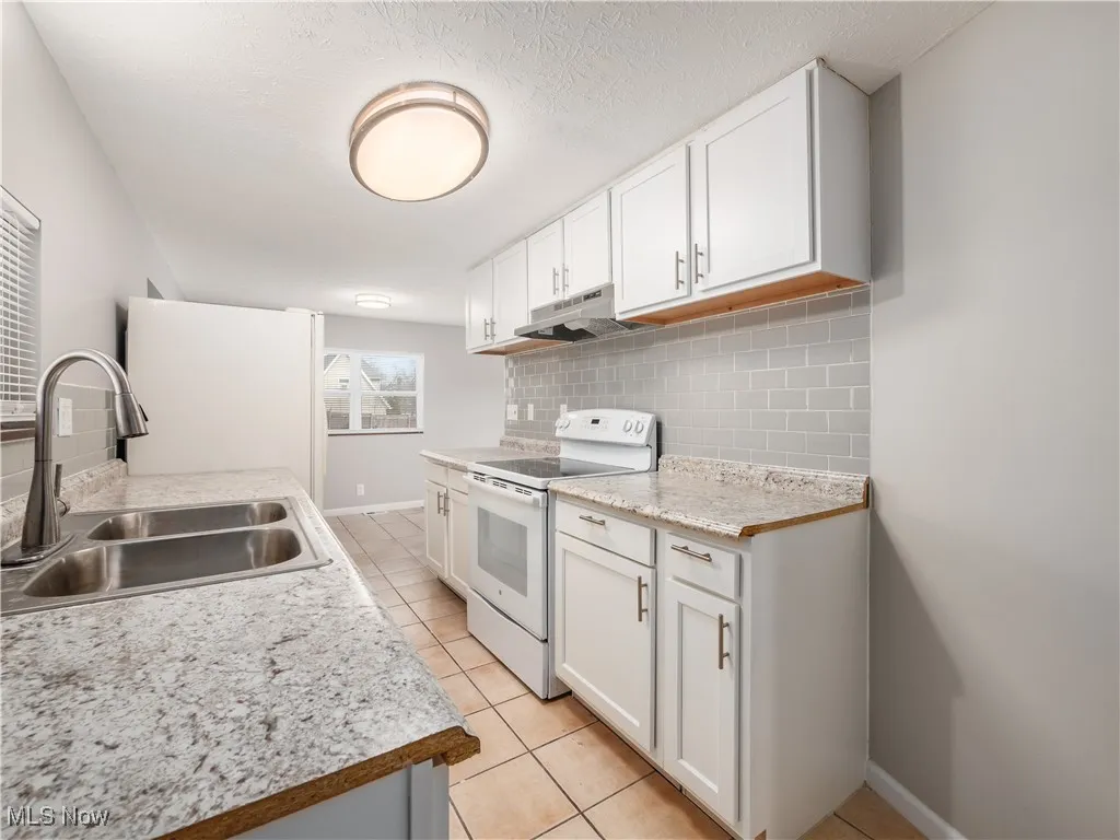 Kitchen with light countertops, white appliances, light tile patterned floors, white cabinetry, and backsplash
