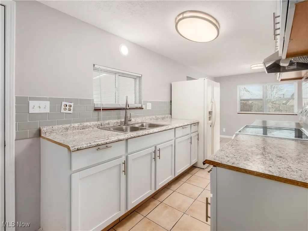 Kitchen featuring light countertops, white cabinetry, white fridge with ice dispenser, light tile patterned floors, and a textured ceiling