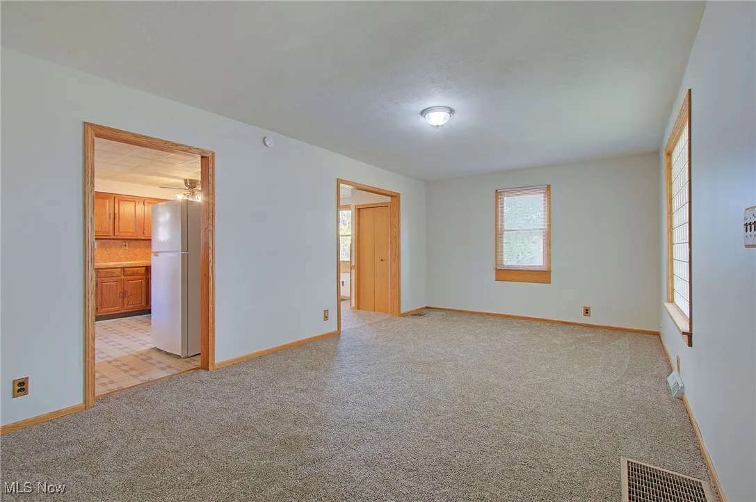 Unfurnished bedroom with freestanding refrigerator and light carpet