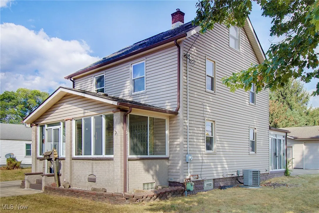 View of side of property with a sunroom, a lawn, a chimney, and brick siding