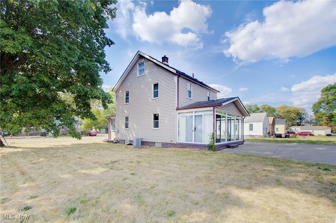 View of side of home featuring a sunroom, a chimney, and a yard