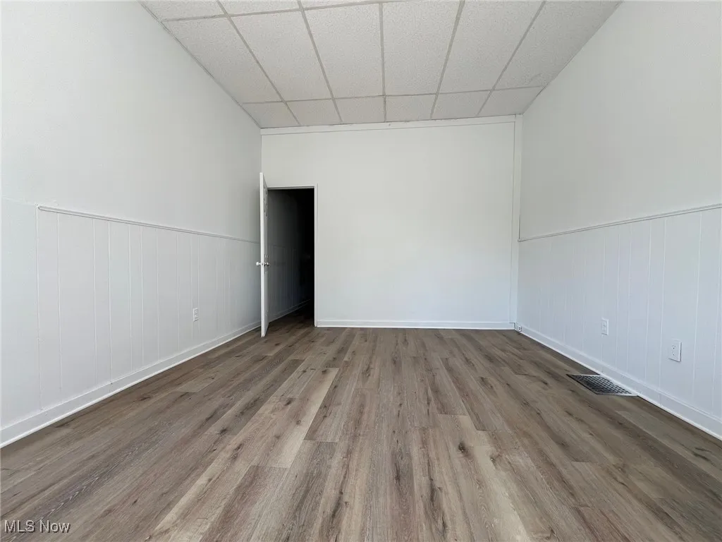 Empty room with a drop ceiling, wainscoting, and wood finished floors