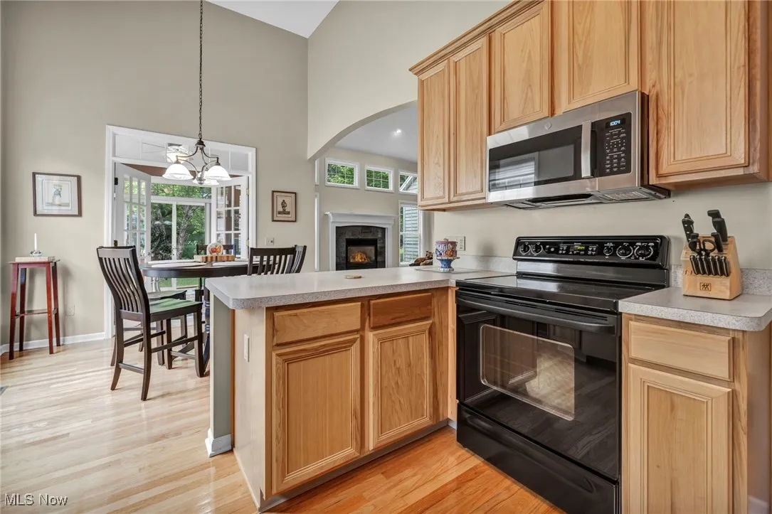 Kitchen with black range with electric stovetop, a peninsula, stainless steel microwave, a high ceiling, and a glass covered fireplace