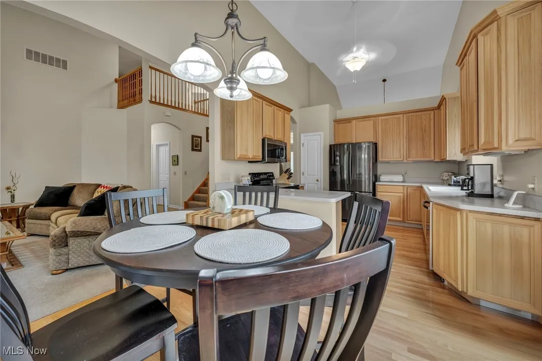 Dining room with light wood finished floors, a chandelier, a high ceiling, stairs, and arched walkways