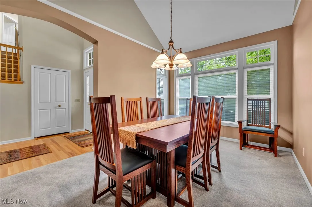 Dining space with arched walkways, a chandelier, high vaulted ceiling, and light carpet