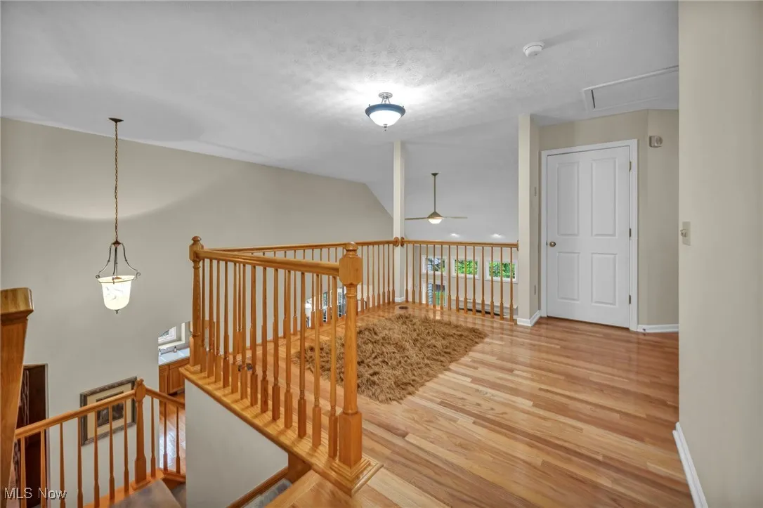 Hall featuring lofted ceiling, light wood finished floors, an upstairs landing, a textured ceiling, and attic access