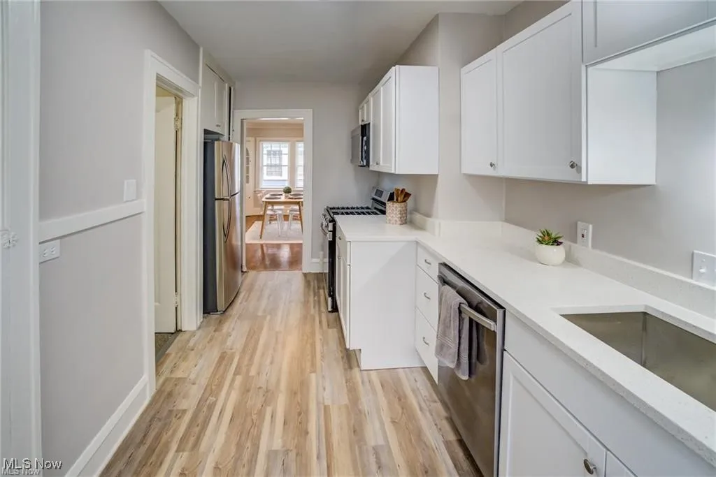 Kitchen featuring light wood-style floors, white cabinets, appliances with stainless steel finishes, and light stone counters