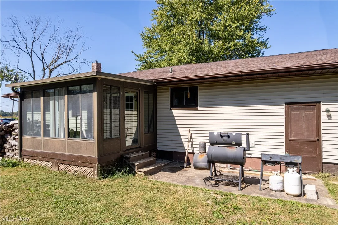 Back of property featuring a lawn, a chimney, a sunroom, a shingled roof, and a patio