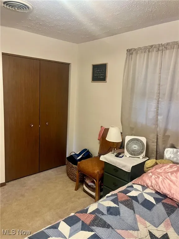 Bedroom featuring a textured ceiling, a closet, and light carpet