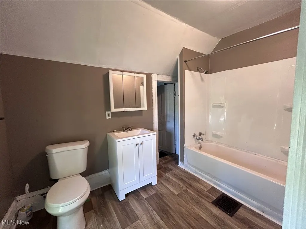 Bathroom with washtub / shower combination, dark wood-style flooring, vanity, and lofted ceiling