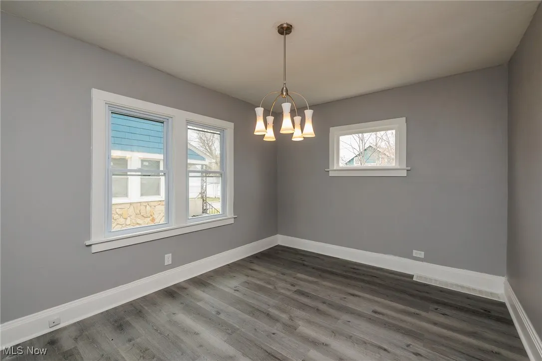 Spare room with dark wood-style flooring and a chandelier