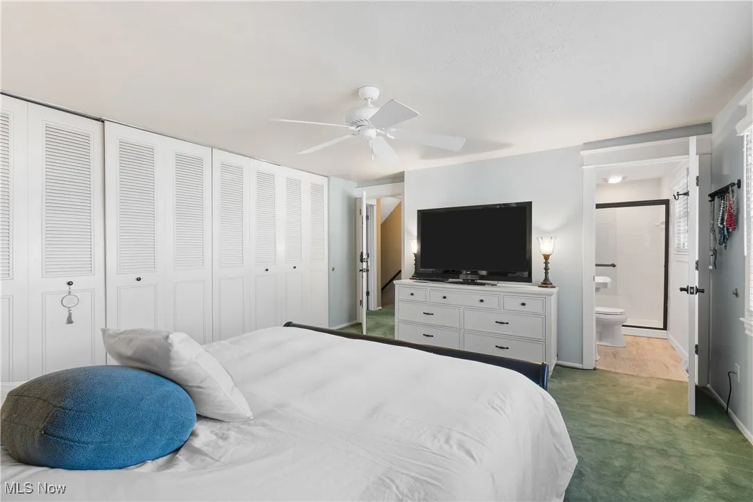 Bedroom with dark colored carpet, a ceiling fan, and connected bathroom
