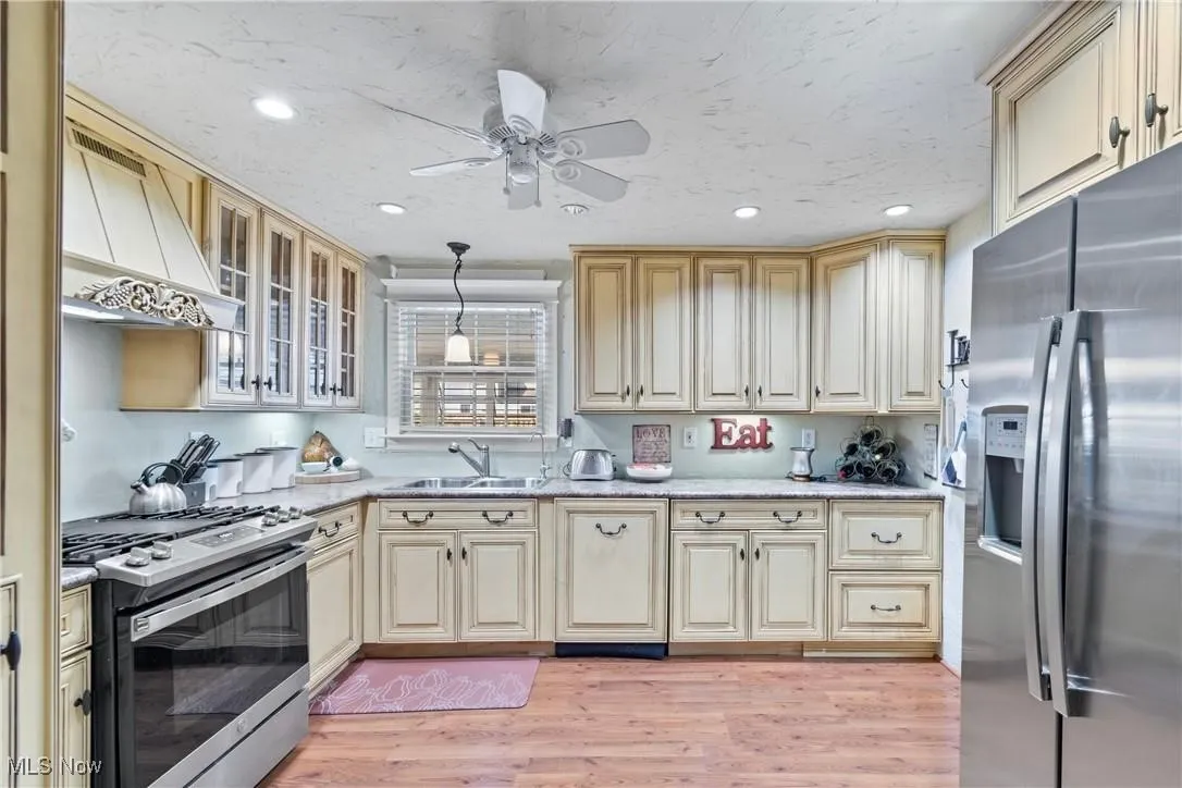 Kitchen featuring appliances with stainless steel finishes, cream cabinetry, light wood-type flooring, premium range hood, and recessed lighting