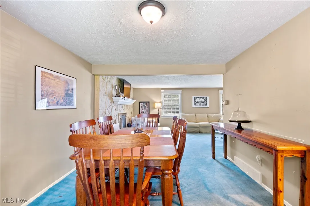 Dining room featuring a textured ceiling, carpet flooring, and a stone fireplace