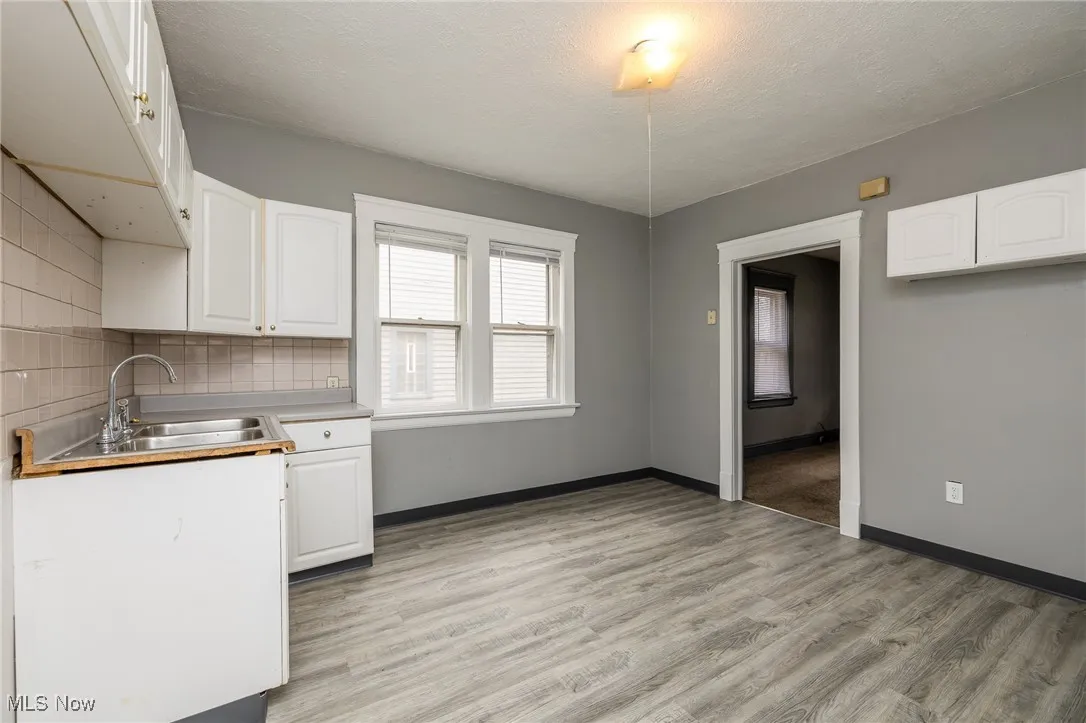Kitchen featuring light wood-type flooring, white cabinetry, decorative backsplash, a textured ceiling, and light countertops
