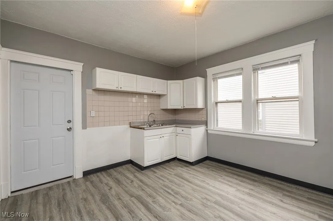 Kitchen with white cabinetry, backsplash, light wood finished floors, and a textured ceiling