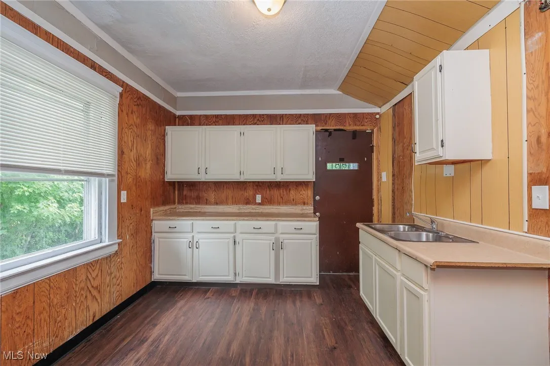 Kitchen with wood walls, light countertops, dark wood-style flooring, white cabinets, and lofted ceiling