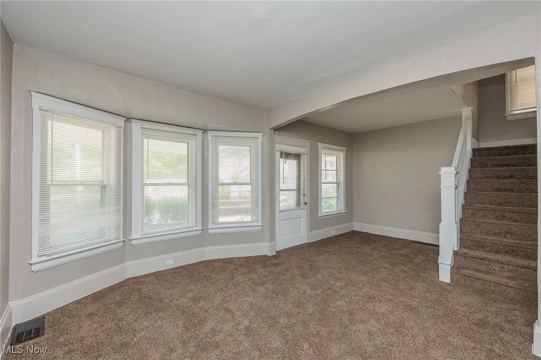 Unfurnished living room featuring stairway, carpet floors, and arched walkways