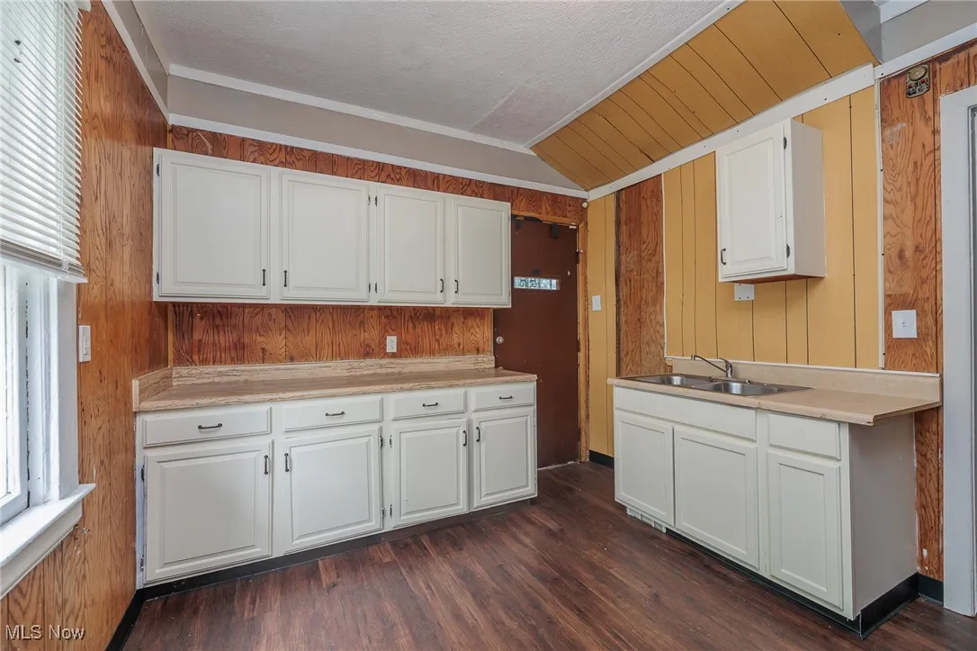 Kitchen featuring vaulted ceiling, light countertops, wooden walls, white cabinetry, and dark wood-style floors