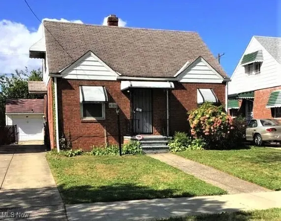 Bungalow with a chimney, brick siding, a front lawn, an outdoor structure, and a garage