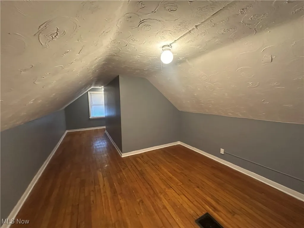 Additional living space featuring dark wood-style floors, a textured ceiling, and vaulted ceiling