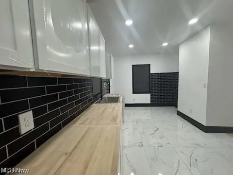 Kitchen with wooden counters, light marble finish flooring, recessed lighting, white cabinetry, and backsplash