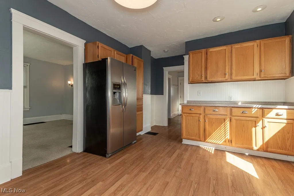 Kitchen with stainless steel fridge, light wood-type flooring, and brown cabinets