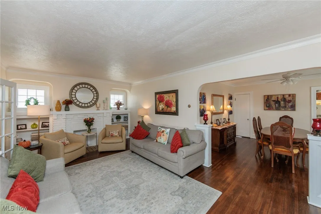 Living room featuring dark wood-style floors, healthy amount of natural light, a textured ceiling, ceiling fan, and crown molding