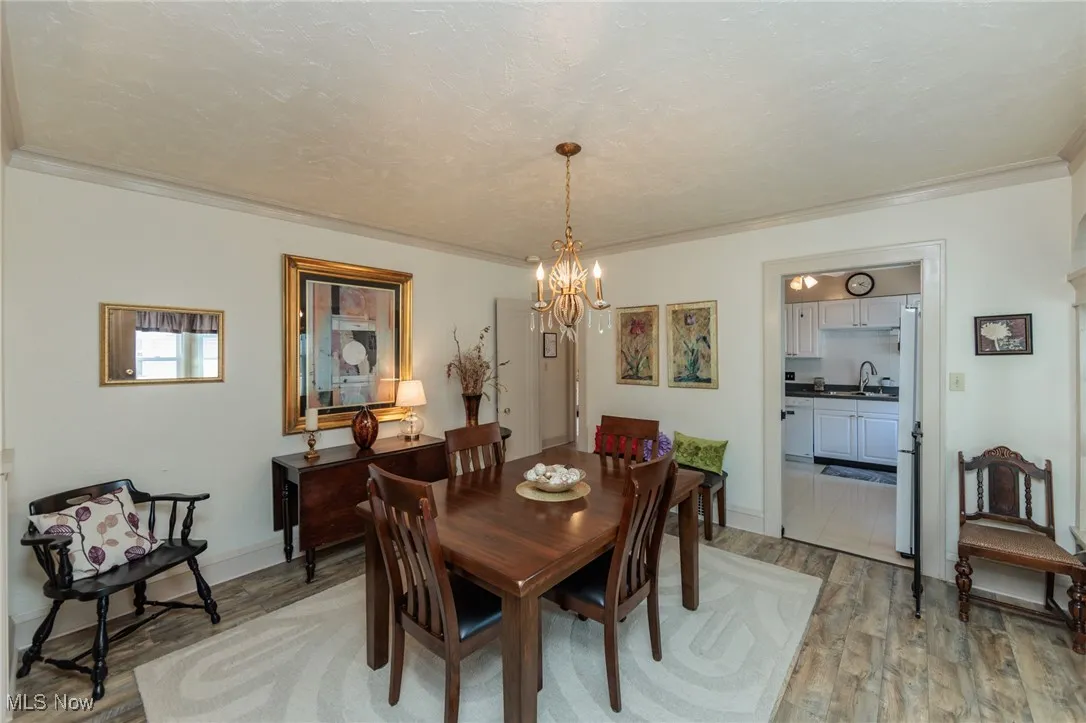 Dining room with light wood finished floors, crown molding, a chandelier, and a textured ceiling