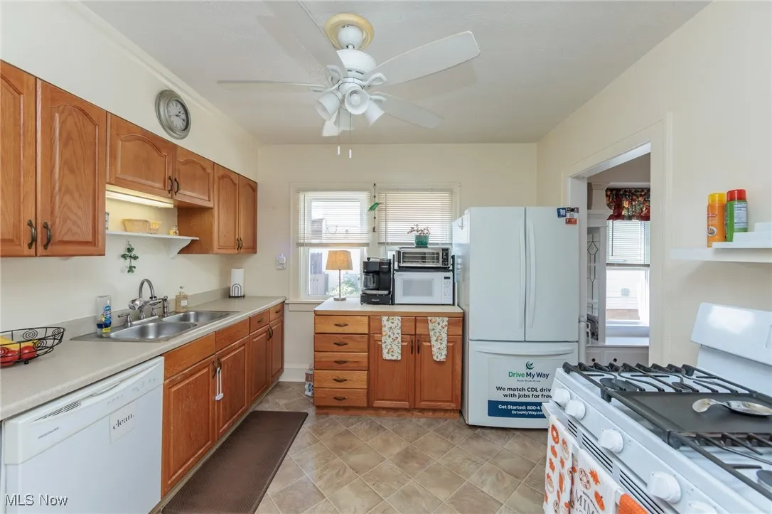 Kitchen featuring white appliances, light countertops, brown cabinetry, and healthy amount of natural light