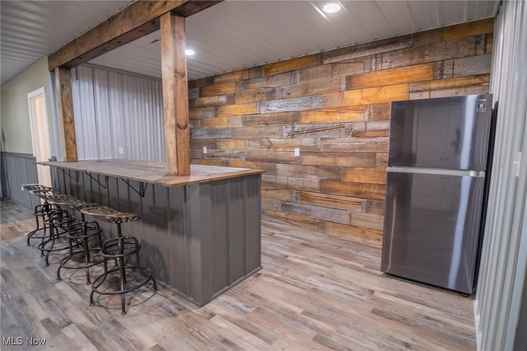 Indoor dry bar with freestanding refrigerator, wood counters, light wood-style floors, recessed lighting, and wooden walls