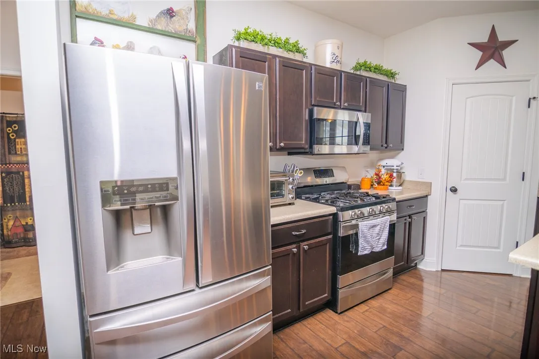 Kitchen featuring appliances with stainless steel finishes, dark brown cabinetry, light countertops, and dark wood-style floors