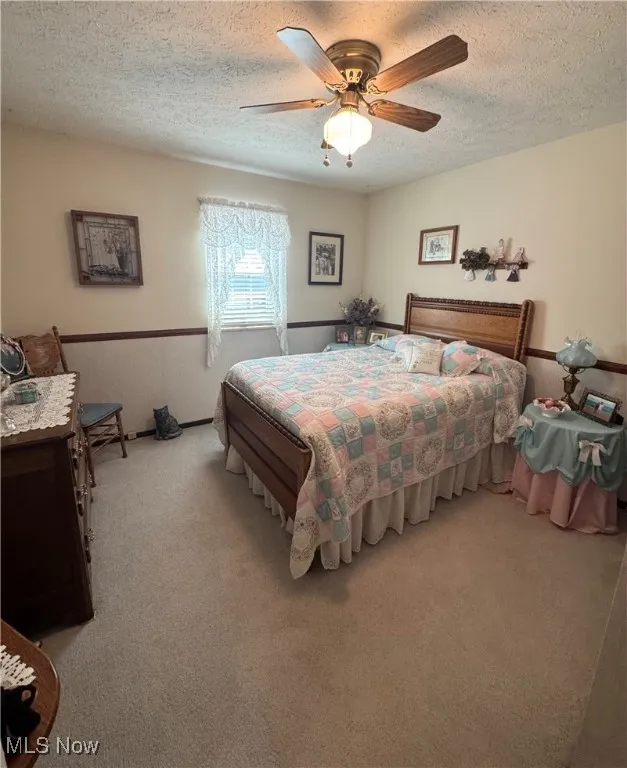 Bedroom with a textured ceiling, light colored carpet, a wainscoted wall, and ceiling fan