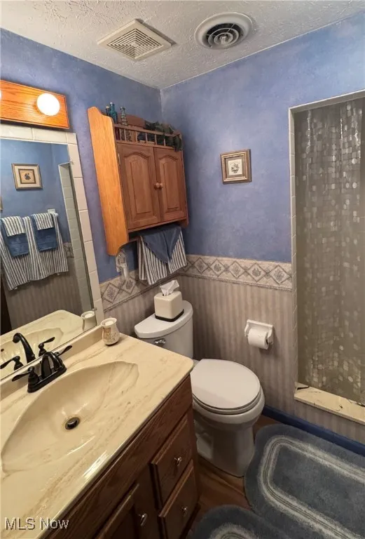 Full bath featuring a textured ceiling, a stall shower, vanity, a wainscoted wall, and dark wood-type​​‌​​​​‌​​‌‌​‌‌​​​‌‌​‌​‌​‌​​​‌​​ flooring
