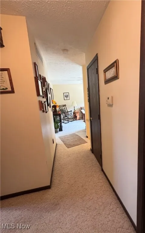 Corridor with light carpet and a textured ceiling