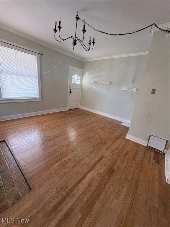 Unfurnished dining area featuring hardwood / wood-style floors, a chandelier, crown molding, and a textured wall