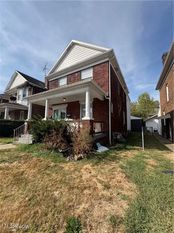 View of front of house featuring a porch, brick siding, and a front lawn