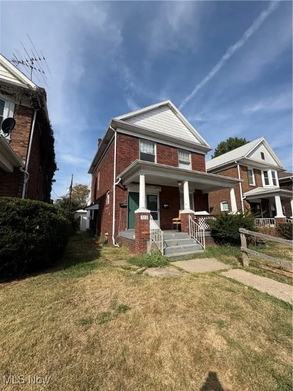 View of front facade with covered porch, brick siding, and a front yard