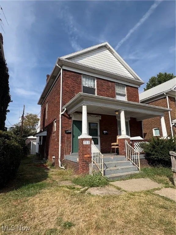 View of front of home featuring covered porch, brick siding, a front yard, and a chimney