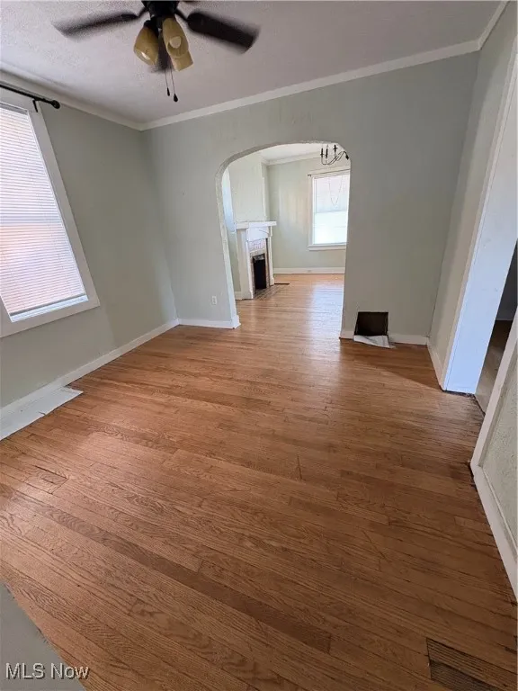 Unfurnished living room featuring crown molding, light wood-style flooring, ceiling fan, arched walkways, and a fireplace
