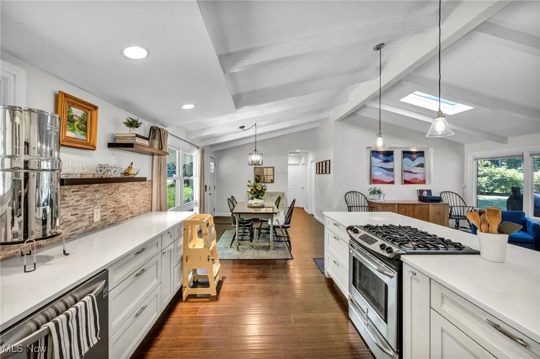 Kitchen with stainless steel appliances, white cabinets, hanging light fixtures, dark wood-type flooring, and light stone countertops