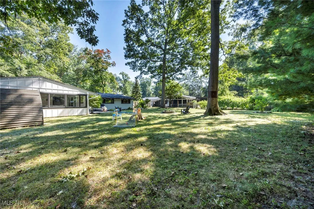 View of green lawn with a sunroom and view of wooded area