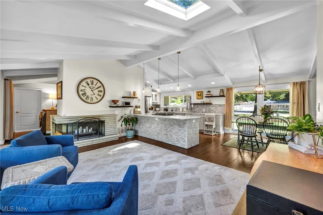 Living room featuring dark wood finished floors, a skylight, a fireplace with raised hearth, and recessed lighting