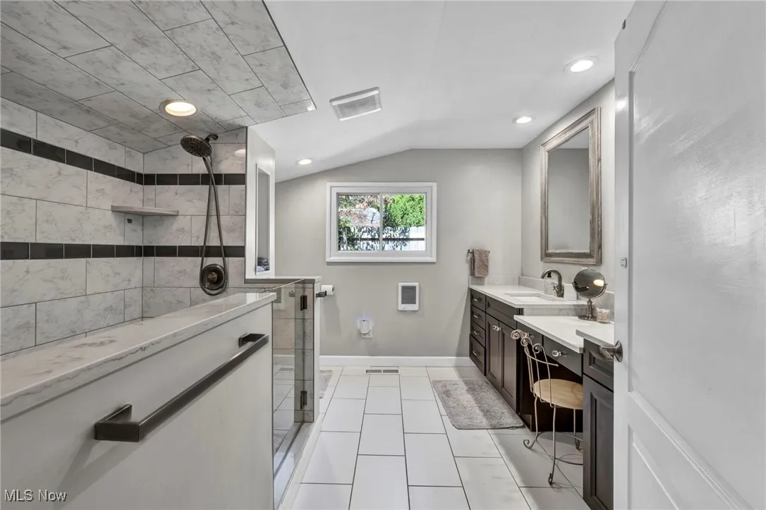 Full bath featuring double vanity, a stall shower, light tile patterned flooring, vaulted ceiling, and recessed lighting