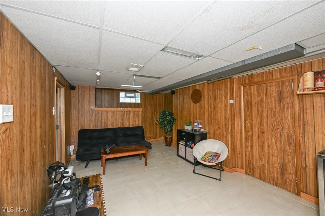 Living area featuring a paneled ceiling, wooden walls, and light tile patterned floors
