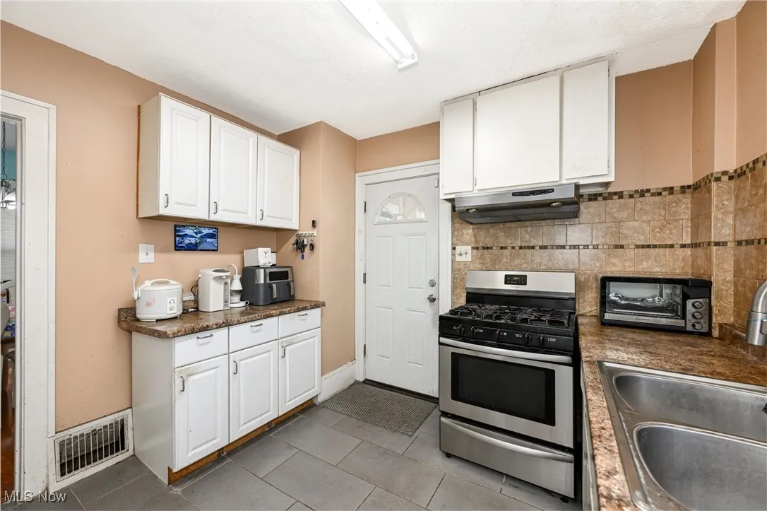 Kitchen featuring gas range, white cabinetry, and dark countertops