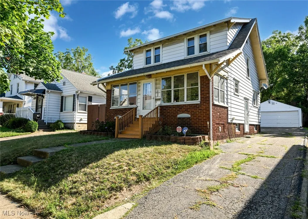 Bungalow featuring an outdoor structure, brick siding, a detached garage, roof with shingles, and a front lawn