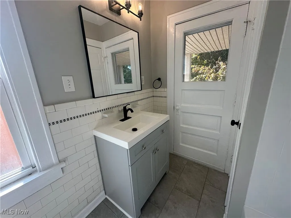 Half bath featuring tile walls, vanity, light tile patterned floors, and a wainscoted wall