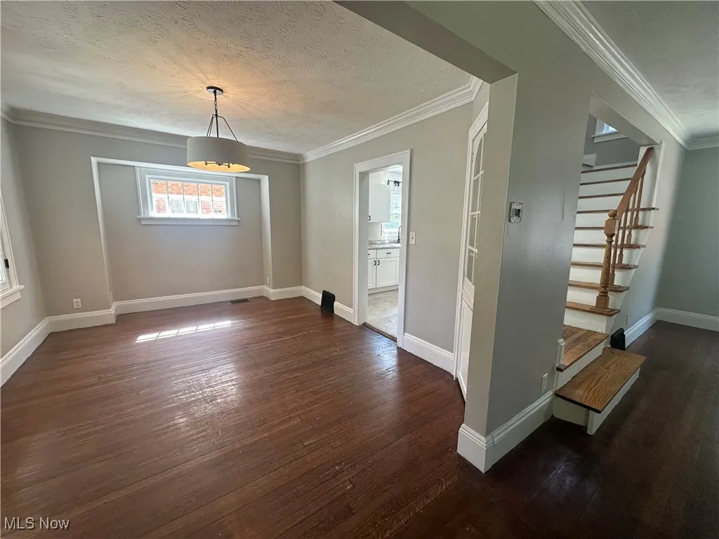 Unfurnished dining area featuring crown molding, dark wood-style floors, a textured ceiling, and stairs